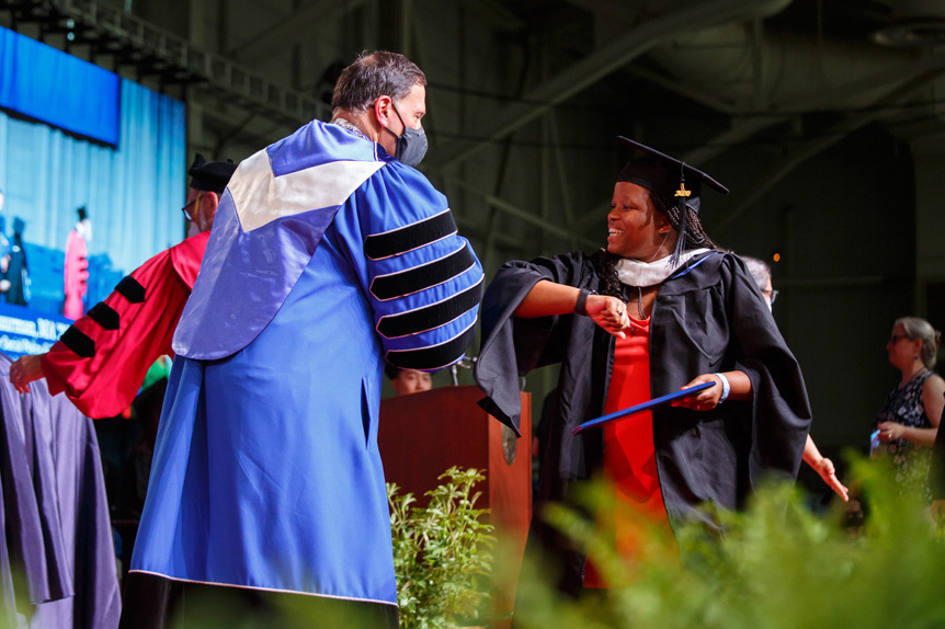 A graduate gives an elbow bump to President Ron Liebowitz