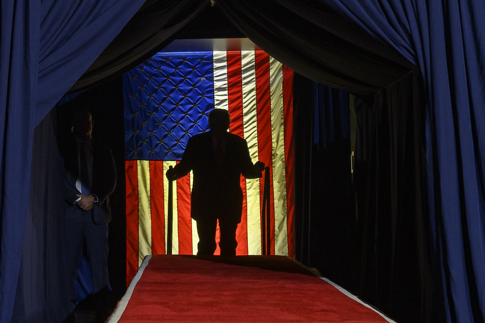 Donald Trump exits a tunnel with an American flag behind him.