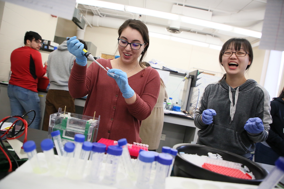 Two biology students laugh as they conduct experiments.