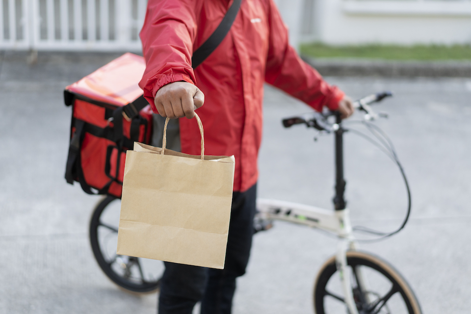 A deliver person on a bicycle holds a paper bag