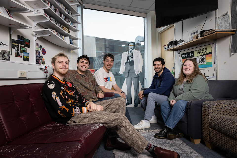 From right to left, members of the WBRS radio station , Kiah Holmstrom ‘25, William Kevorkian ‘23, Joshua Hertz ‘24, Saul Goldstein ‘23, and Ellis Zehnder ‘23 pose for a photo in the WBRS studio