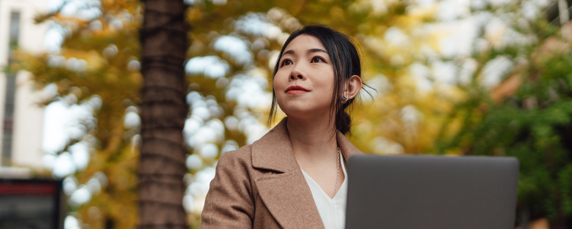 Woman looks up at the trees, while using her laptop.