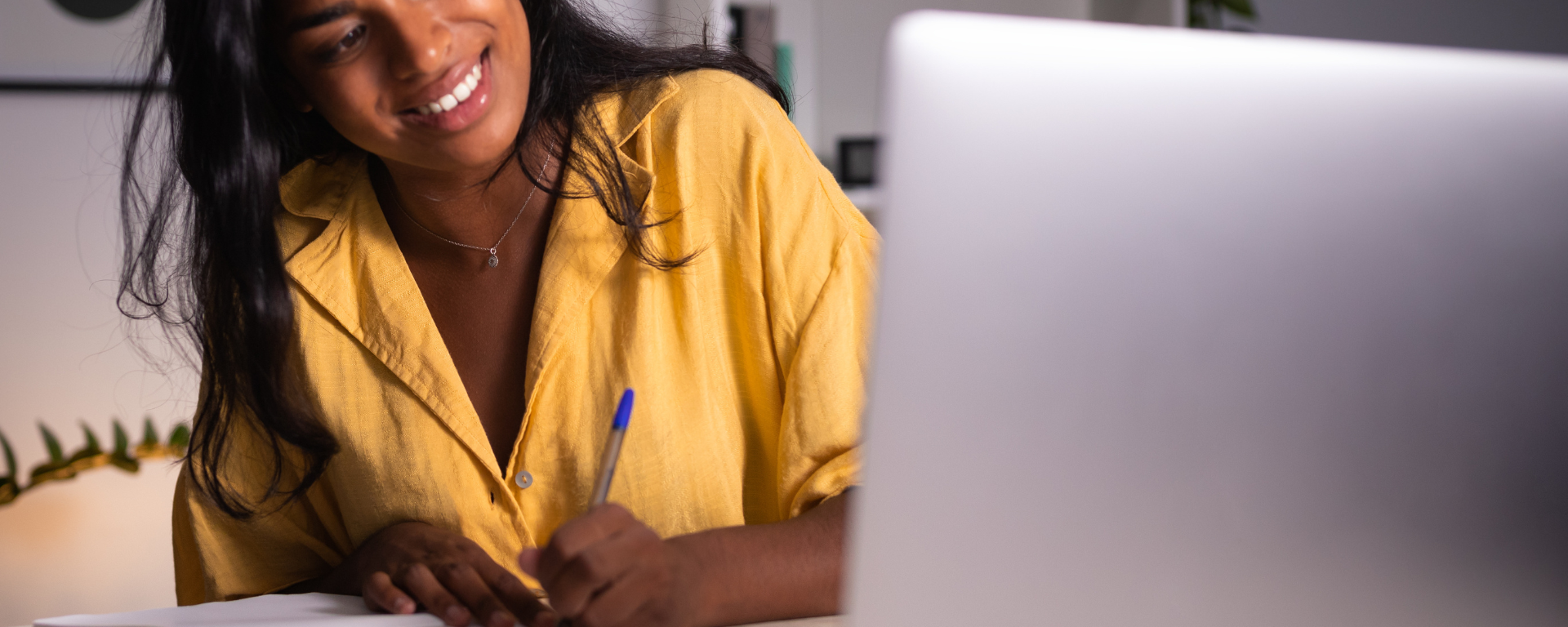 woman writing notes while looking at her computer