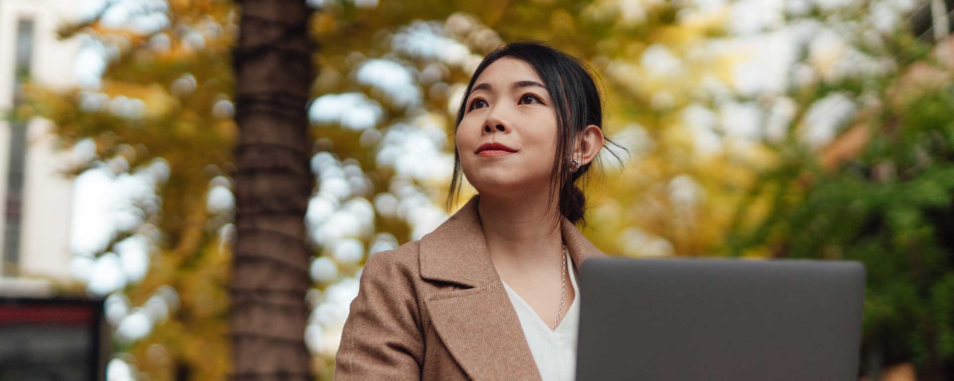 Woman looks up at the trees, while using her laptop.