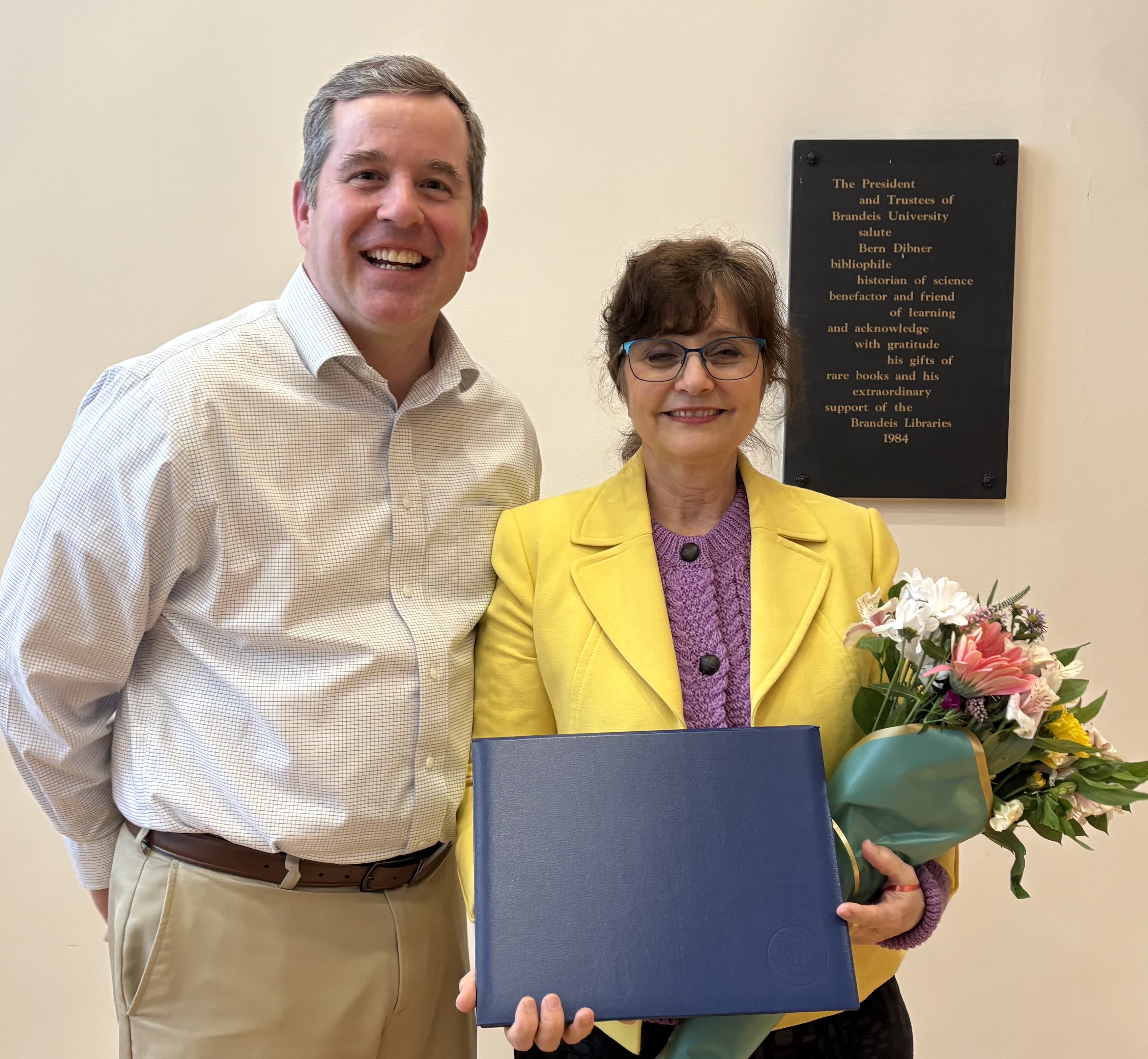 Dr. Anna Shebanow stands next to Assistant Dean of Education & Learning Innovation, holding a bouquet of flowers and an award certificate in her hands.