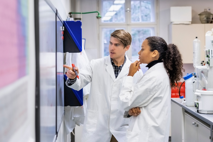 Two people in labcoats looking at results being projected on the wall