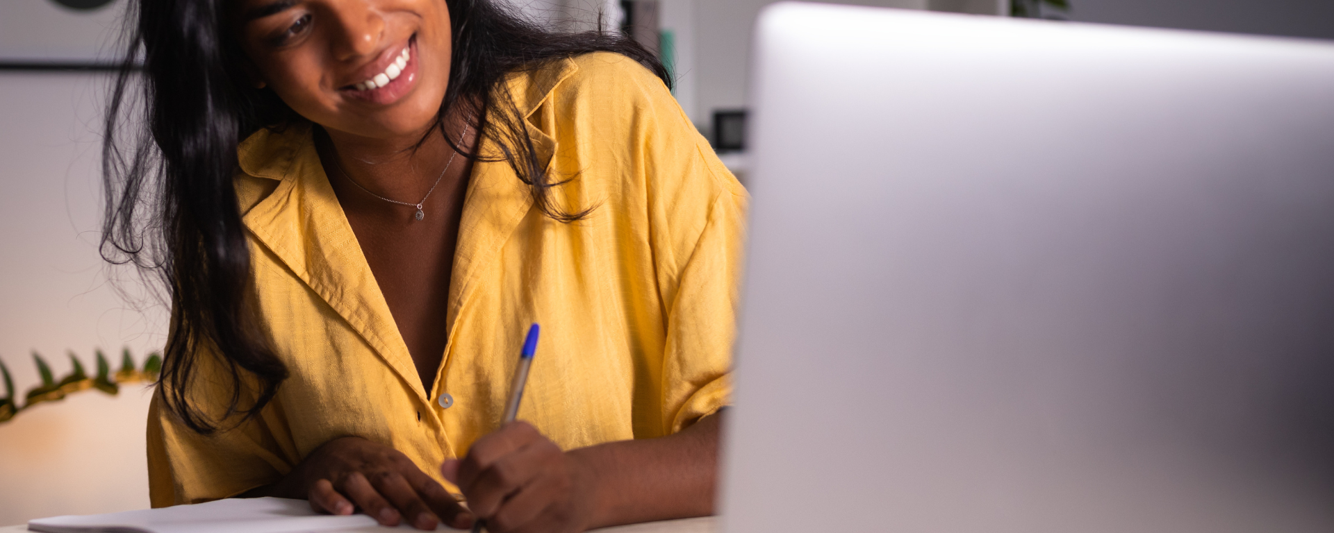 Woman writes in notebook while looking at computer