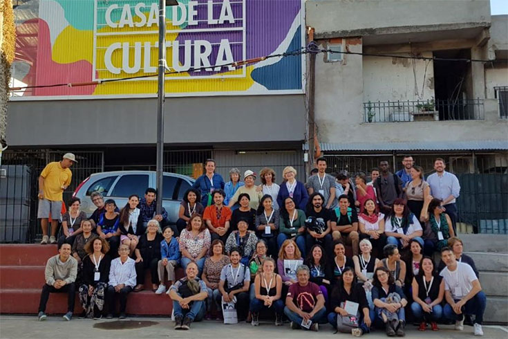A large group of people sits in front of Casa de la Cultura