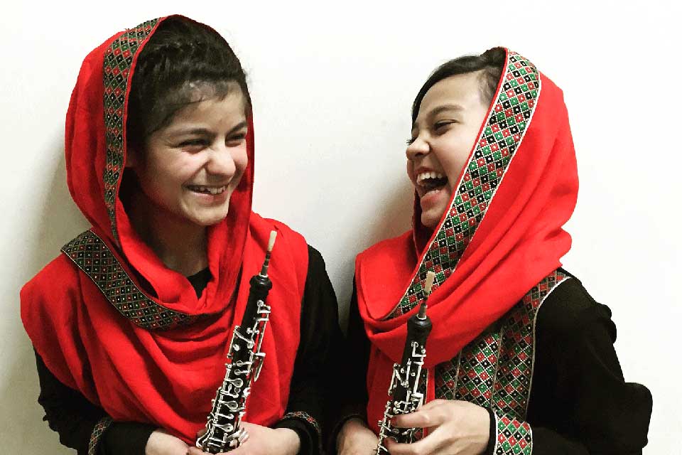 Two girls with scarves on their heads hold oboes and laugh together
