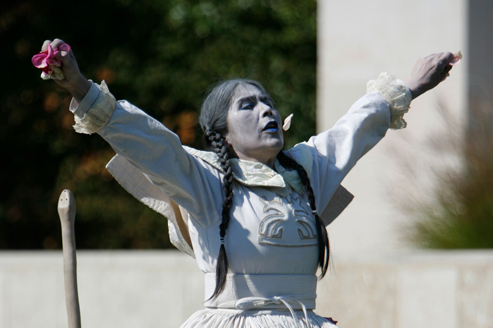 A performance artist raises their hands in the air and looks to the sky