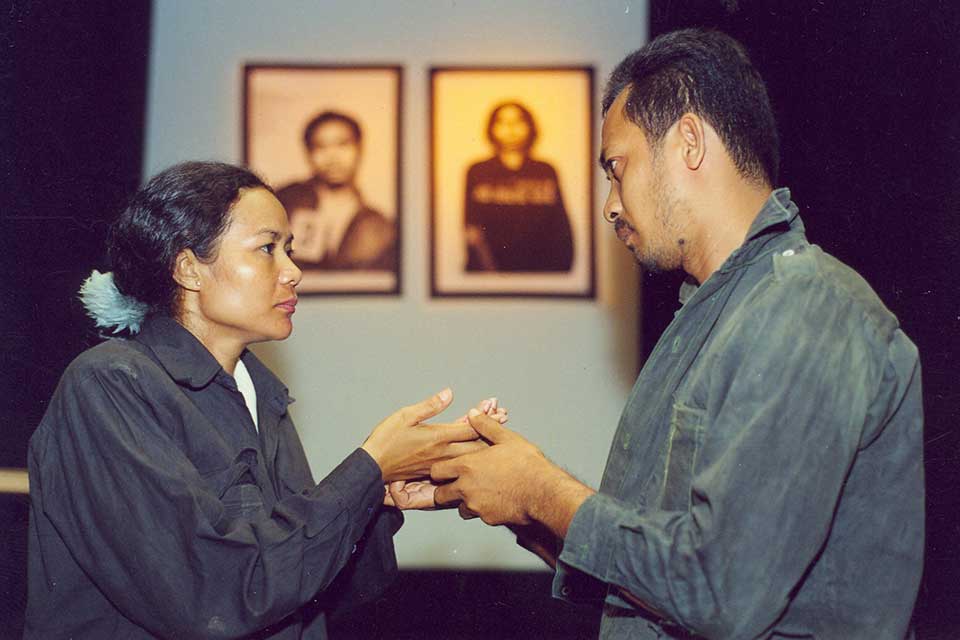 Two actors hold hands and look into each others' eyes. 