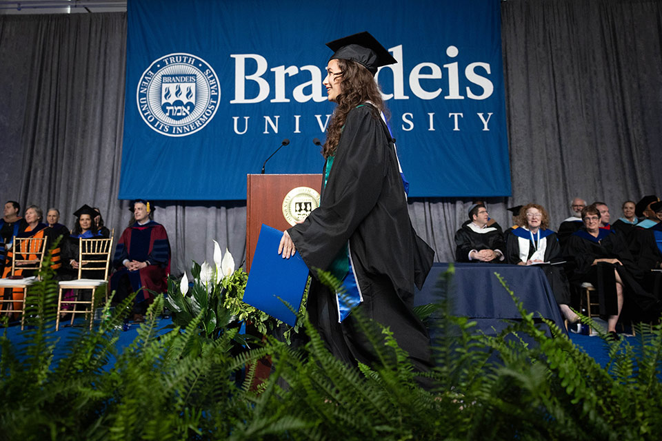 A graduate in a cap and gown walks across the stage during Commencement