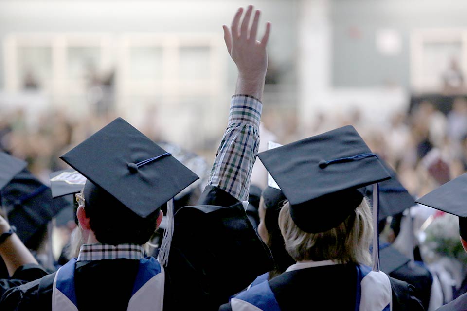 Students at Commencement, one with a hand raised