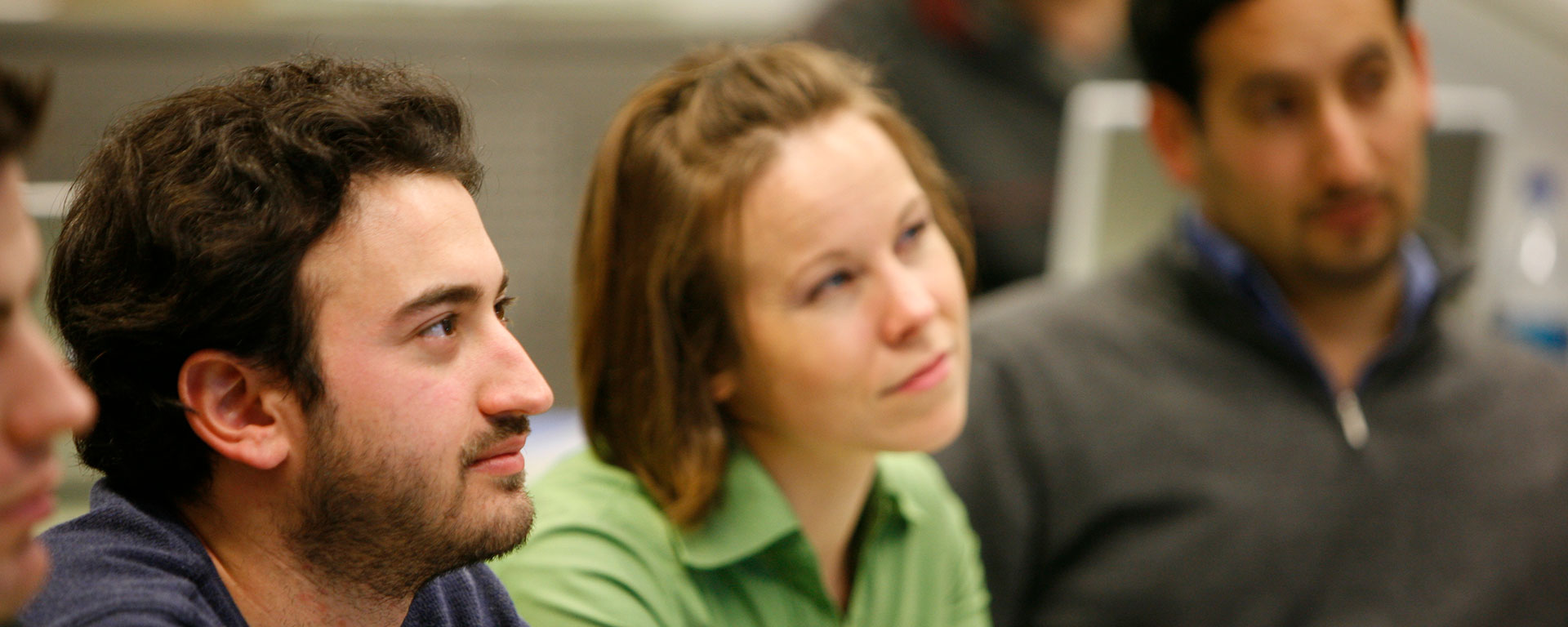 Students sit and listen to a professor at the front of the room.