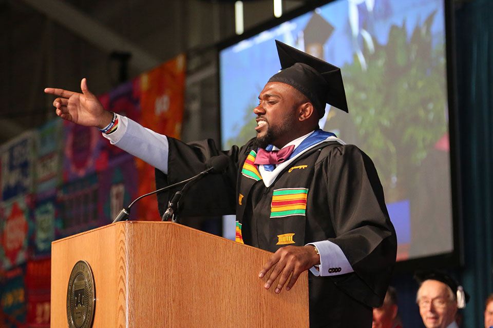 Joel Burt-Miller speaks at a podium wearing a cap and gown