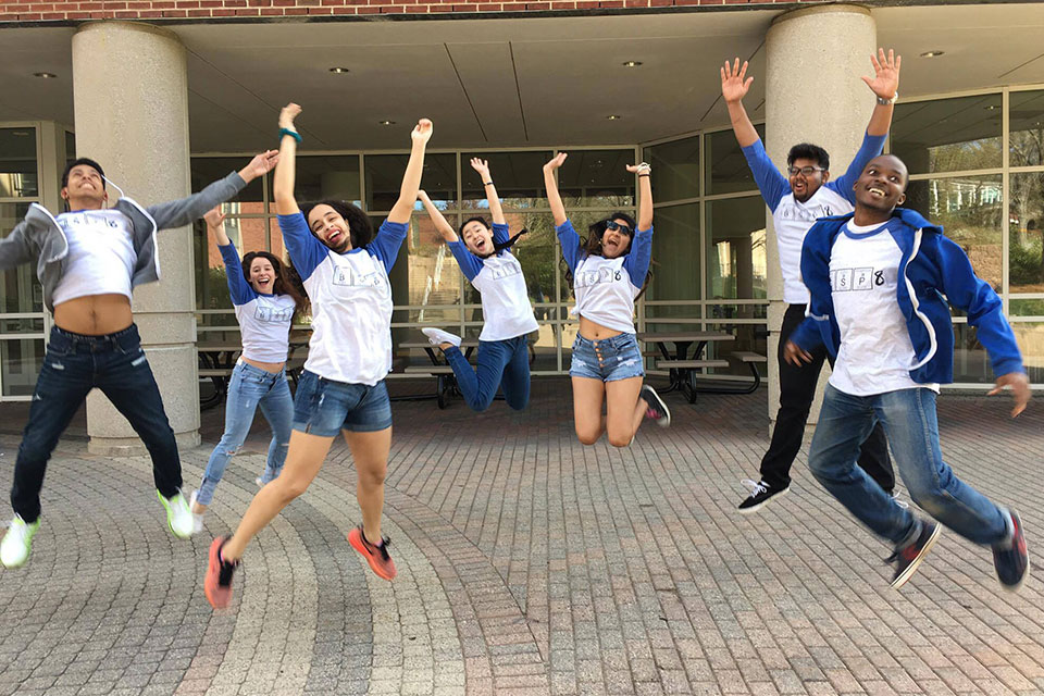 A group of students wearing matching shirts all jump in the air