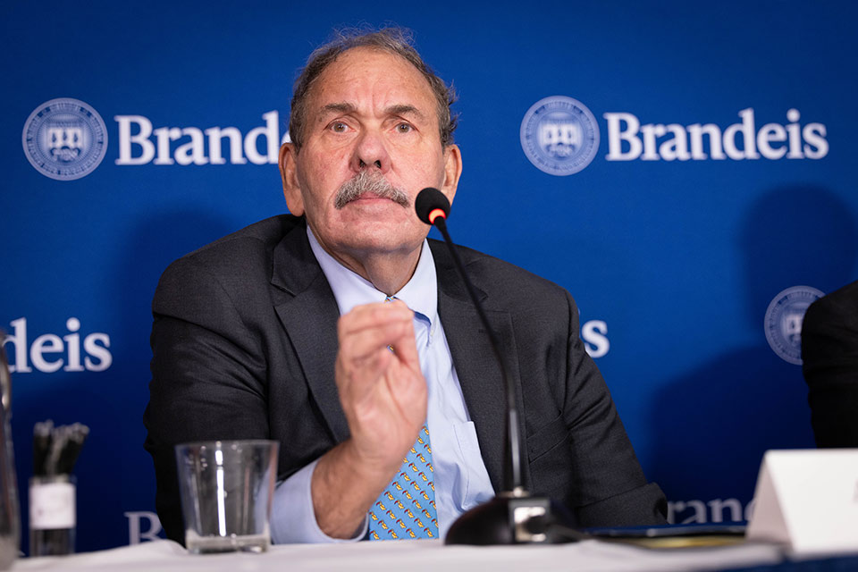 Arthur Levine speaks into a microphone, a Brandeis backdrop is seen in the background