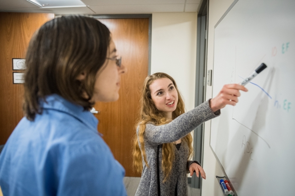 Student writing on a whiteboard with Prof. Snyder