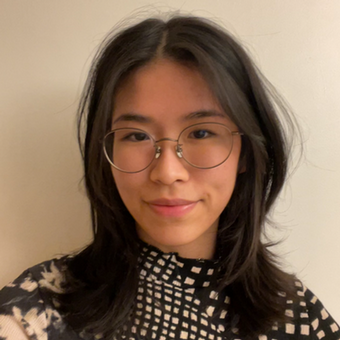 a young girl with shoulder length dark hair and glasses. this is a headshot with a blank wall in the back