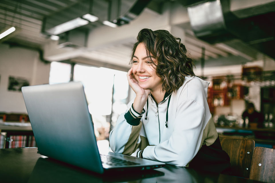 A student smiles looking at a laptop screen