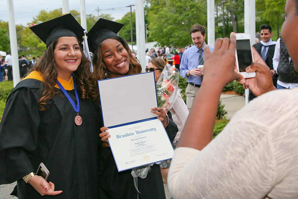 Two graduates having their photo taken. One is holding a diploma