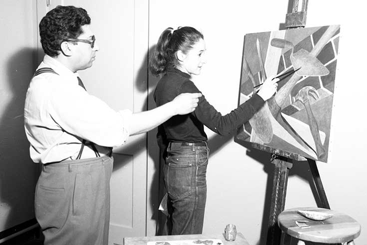 Black and white photo of two people looking at a canvas painting