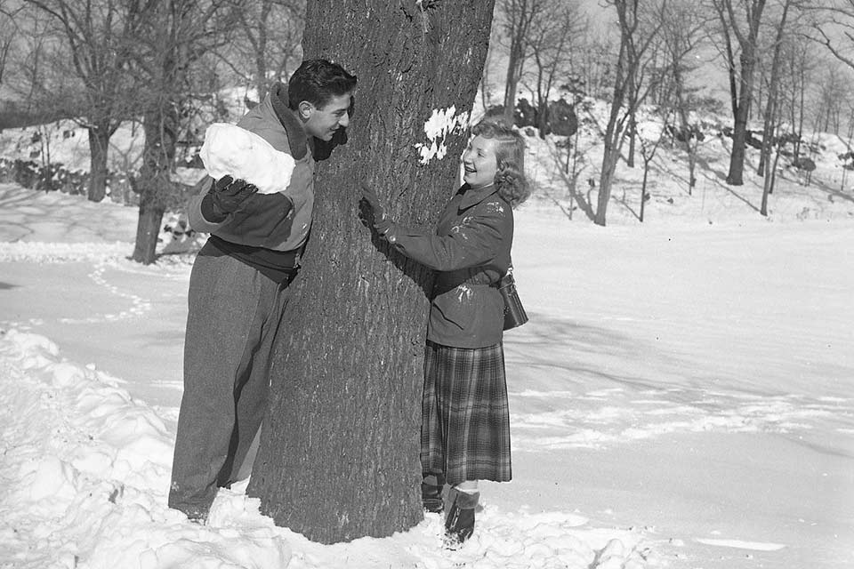 Black and white photo of two people near a tree in the snow