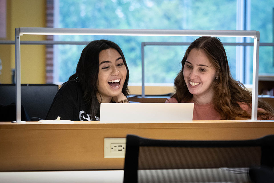 Two students smile while studying in the library