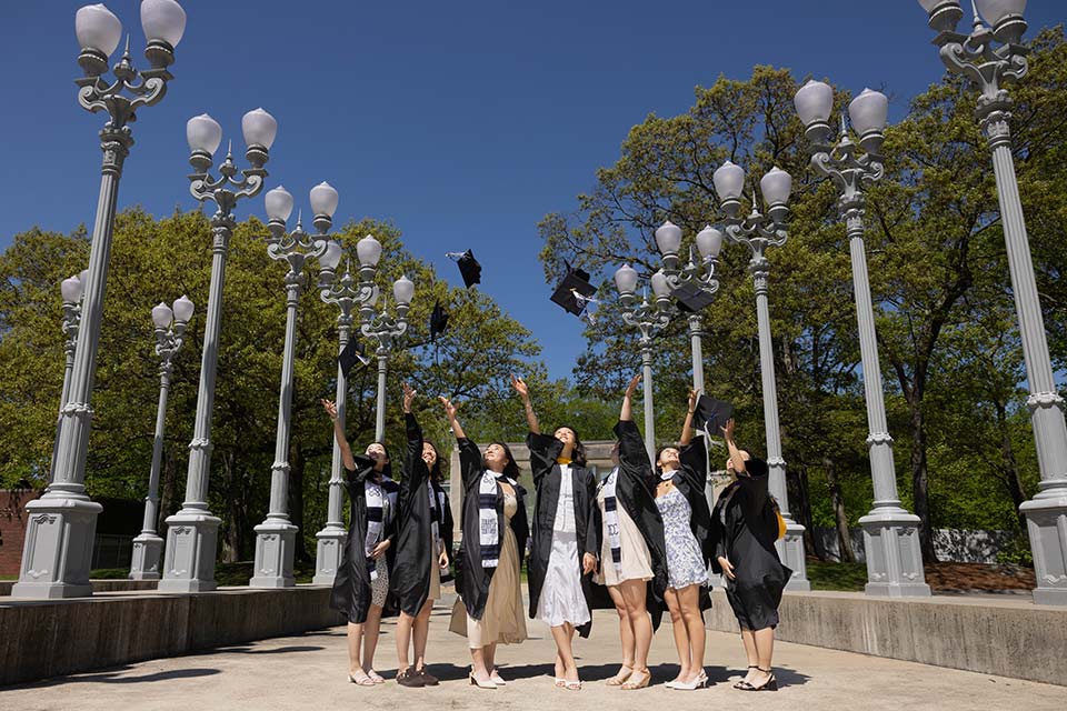 Several students in caps and gowns toss their caps in the air by the Light of Reason