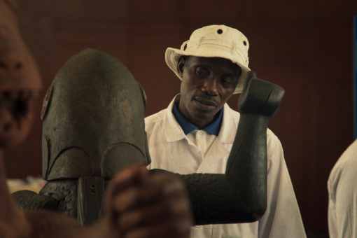 African man wearing a white hat looks at a statue in foreground