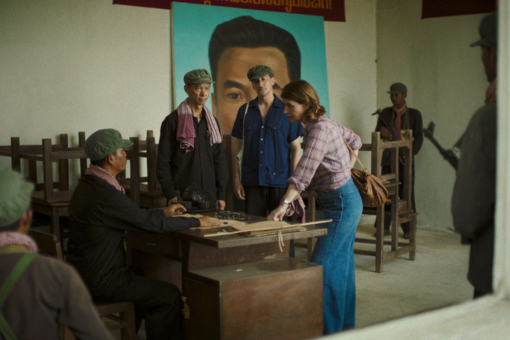 A woman leaning on a man's desk and talking