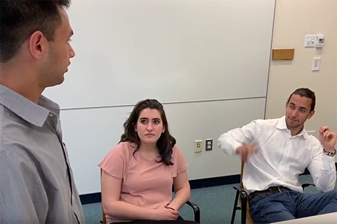 two male students and a female student talking, sitting at a table in a conference room