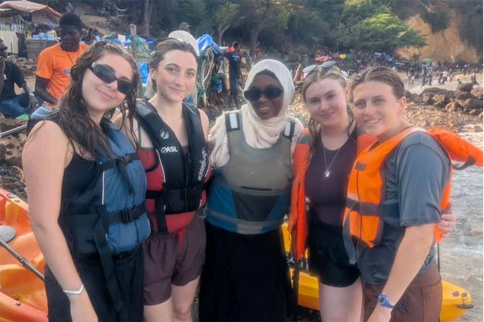 Five people standing on a beach wearing life jackets.