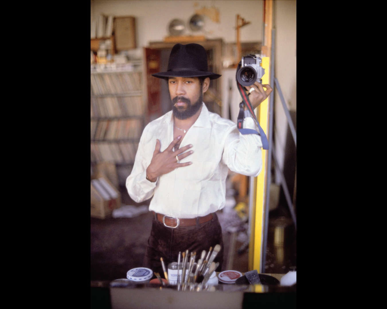 Self-portrait of artist Barkley Hendricks wearing a black hat and holding a camera