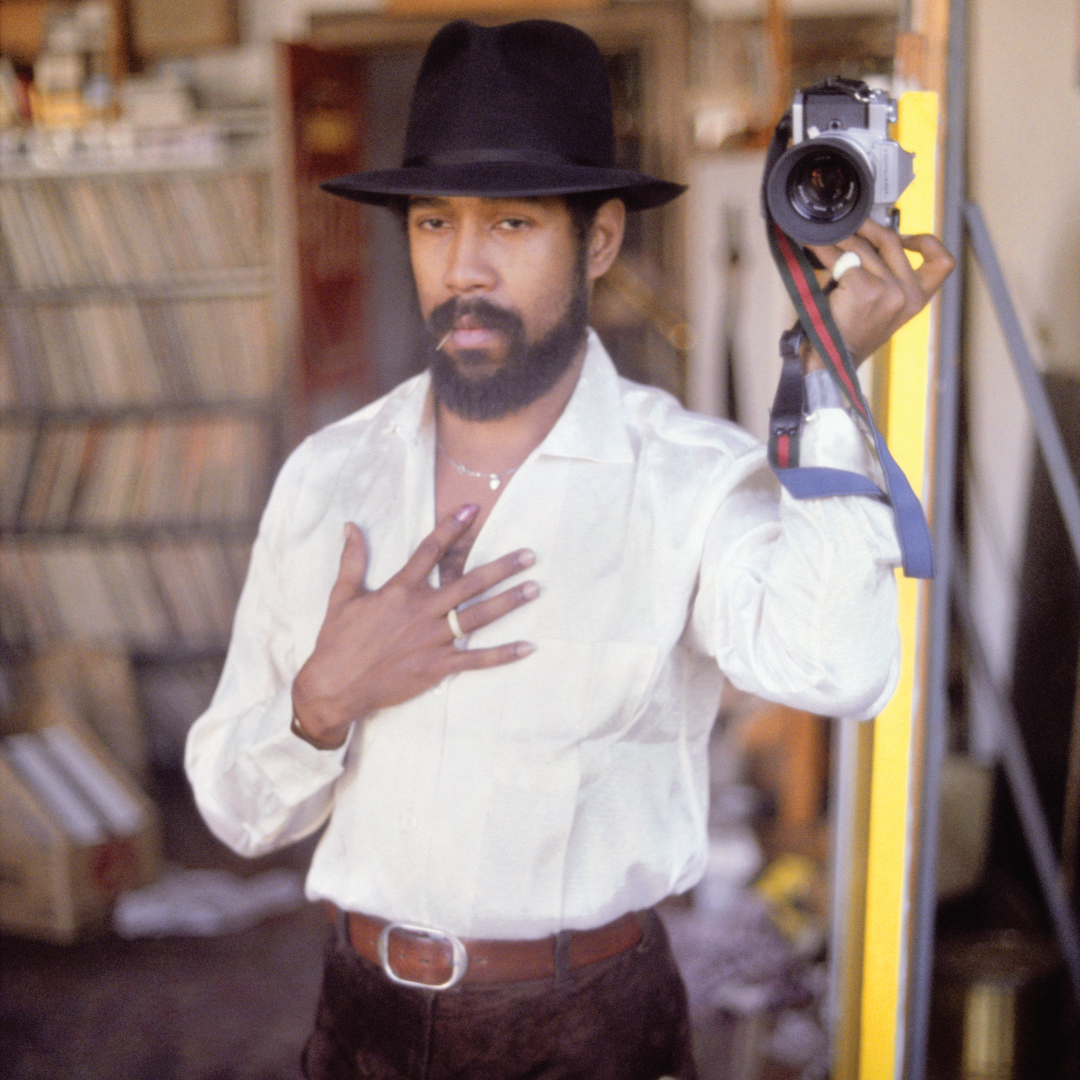Self-portrait of artist Barkley Hendricks wearing a black hat and holding a camera