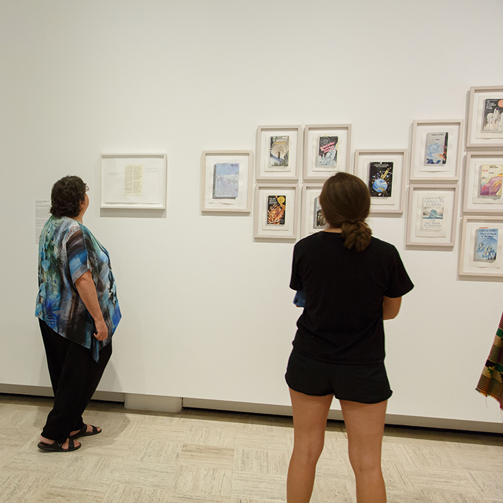 People in galleries looking at Tuesday Smillie's series of Le Guin book covers