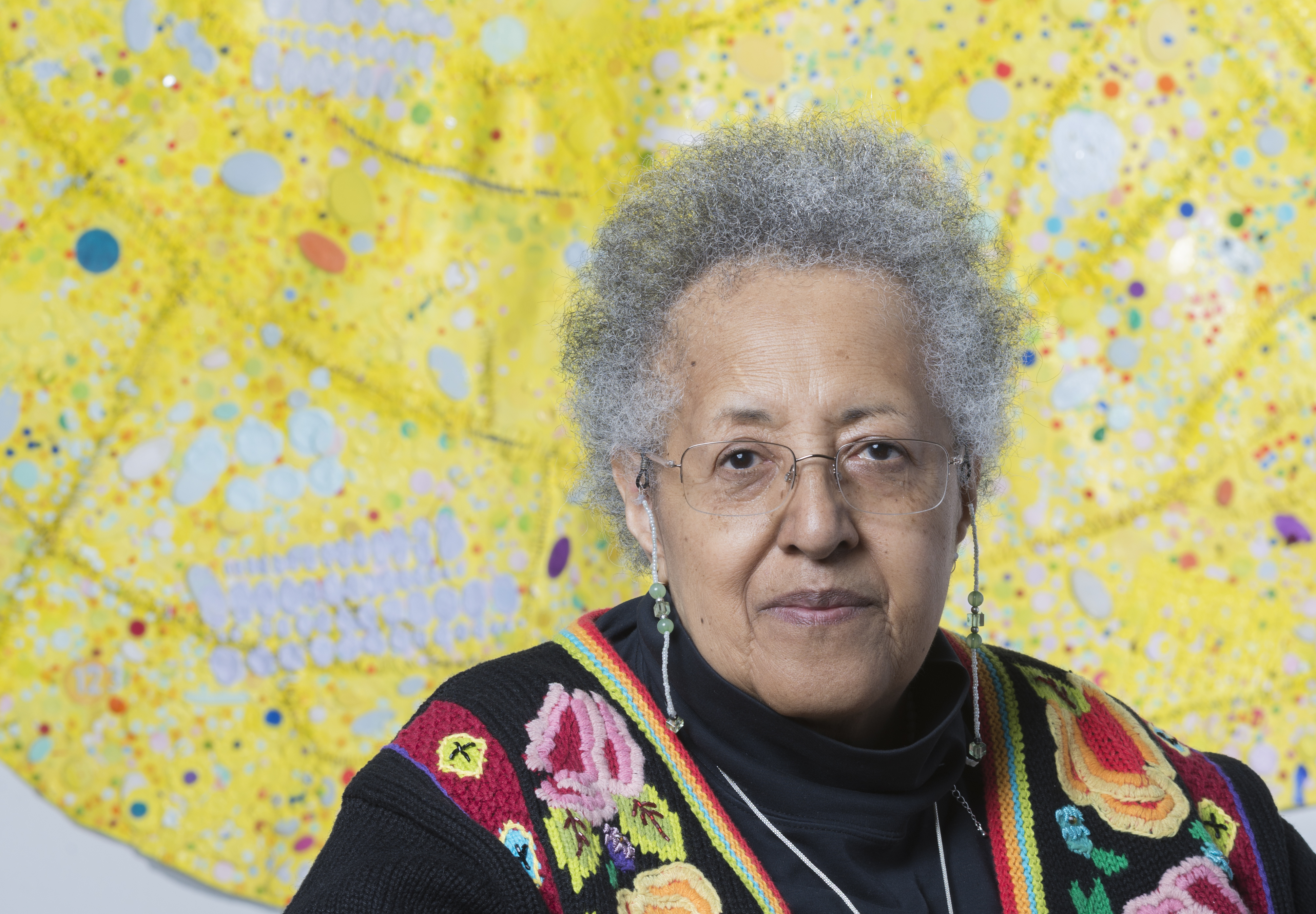 Headshot of artist Howardena Pindell in front of one of her works