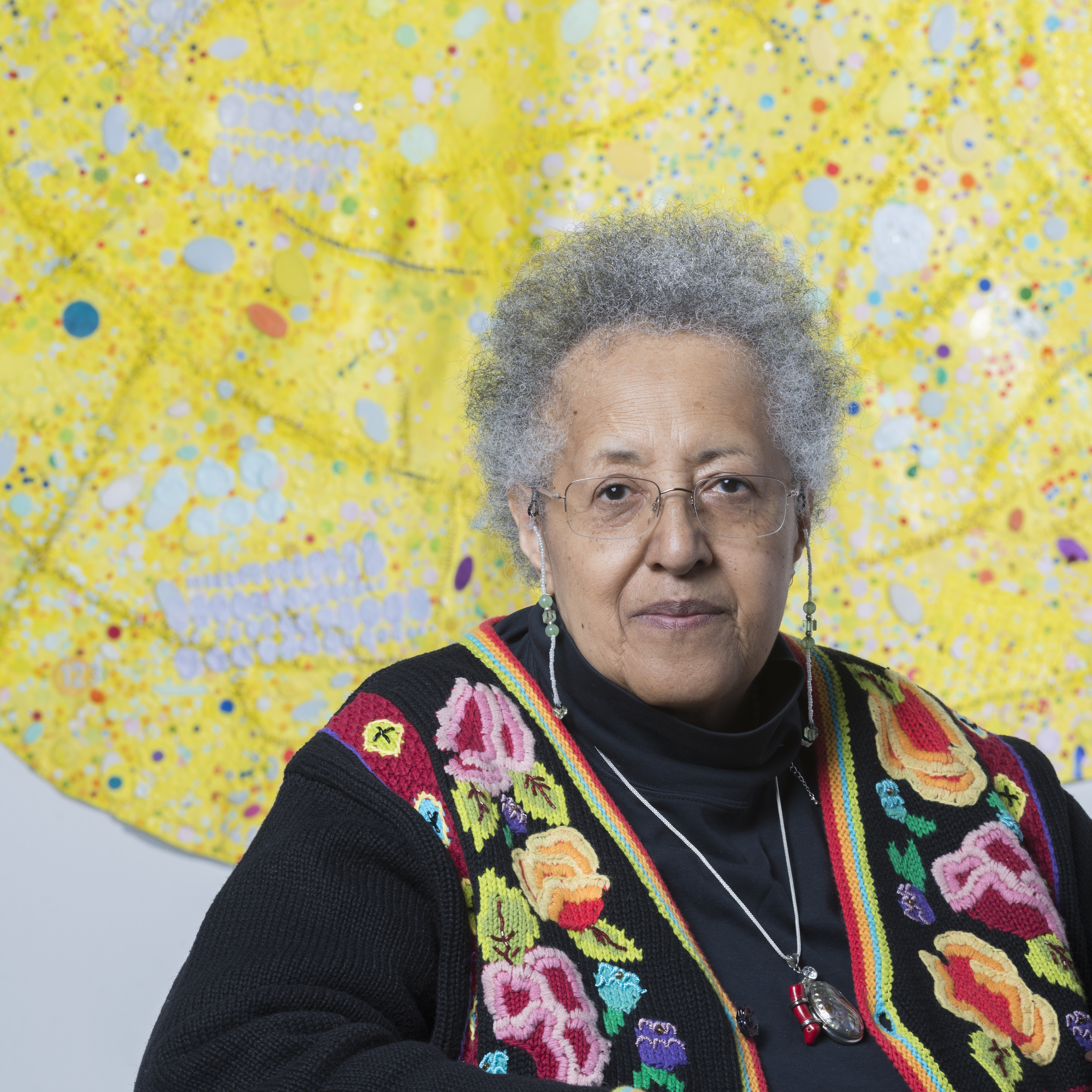 Headshot of artist Howardena Pindell in front of one of her works
