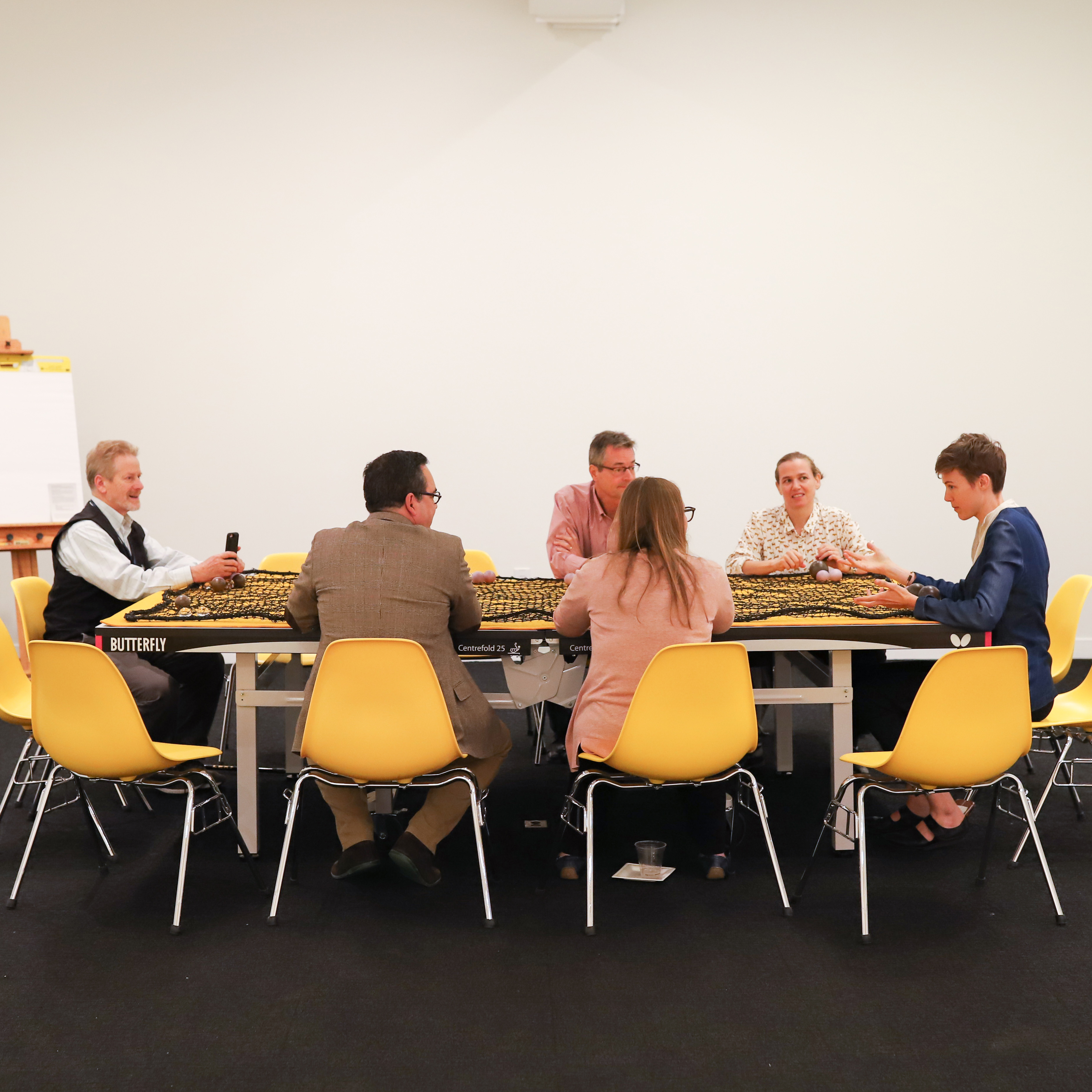 People sitting around a yellow table in yellow chairs talking 