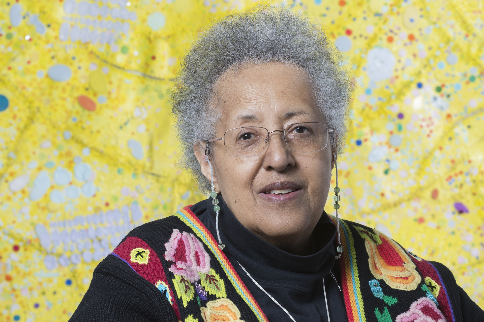 Head shot of Howardana Pindell in front of one of her paintings, a bright yellow abstraction