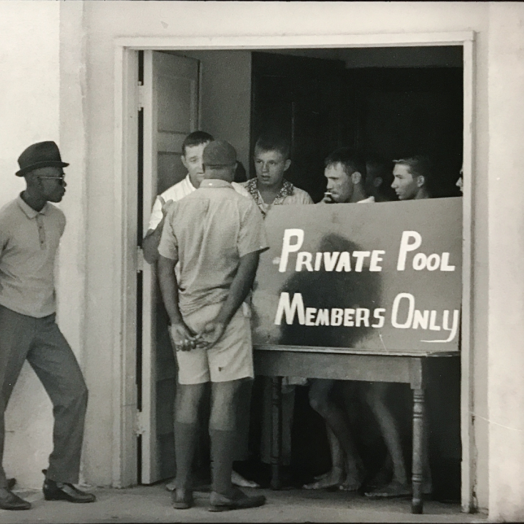 Photograph by Danny Lyon of white young men blocking Black men from using a swimming pool