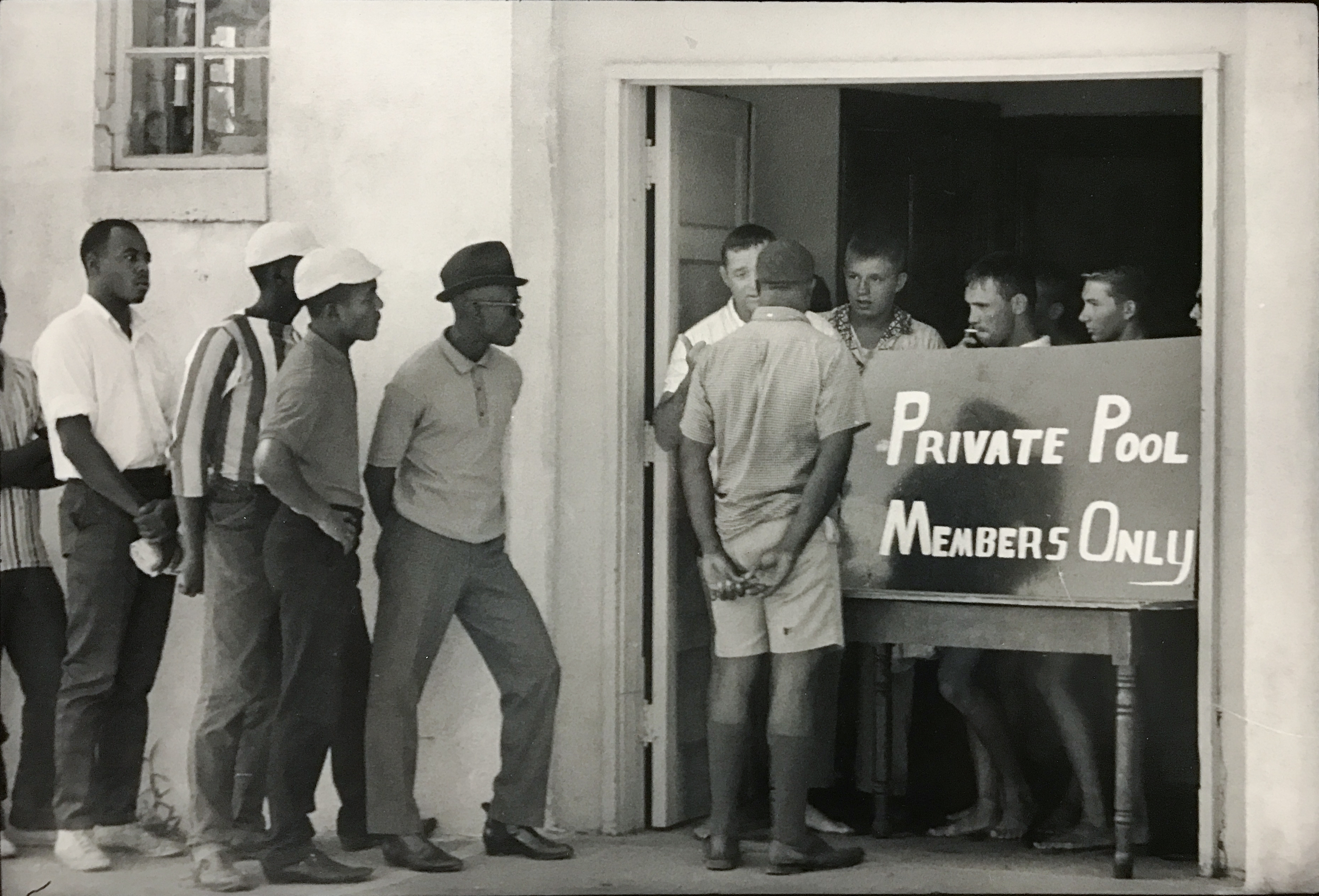 Photograph by Danny Lyon of white young men blocking Black men from using a swimming pool