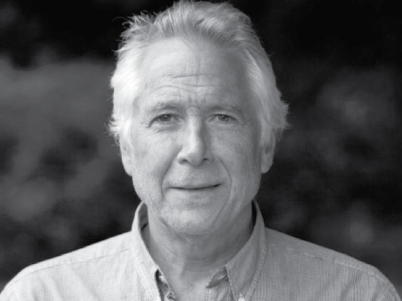 Black and white photo of a white man with white hair wearing a collared shirt.