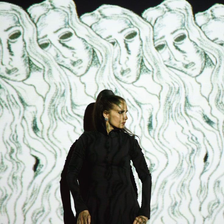 A woman in a black dress stands in front of a screen with animated drawings