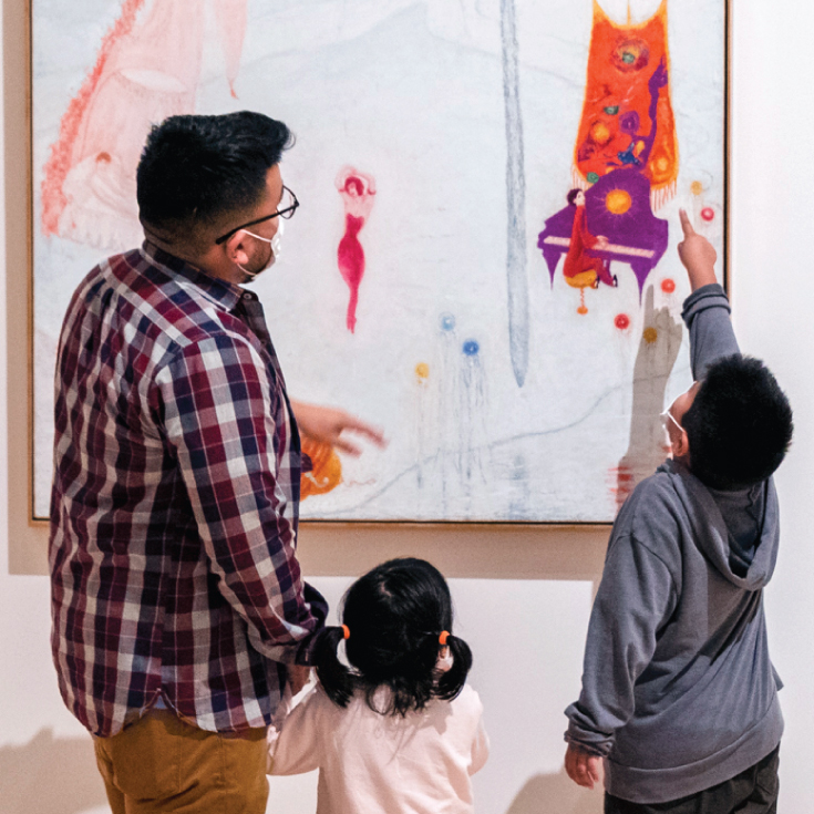 A father and two children look at a painting.