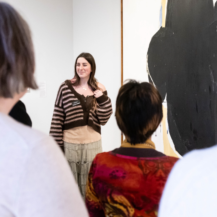 A Brandeis student discusses a painting with a group of visitors.