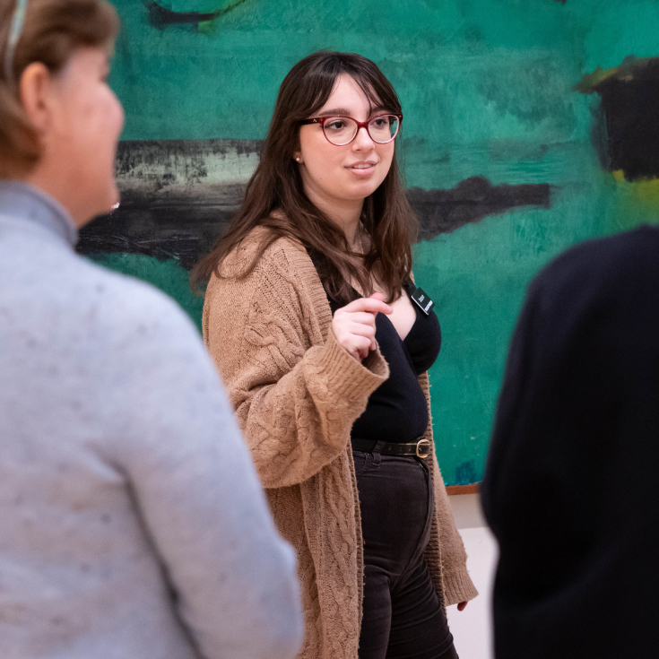 A student docent discusses a painting with a group of visitors.