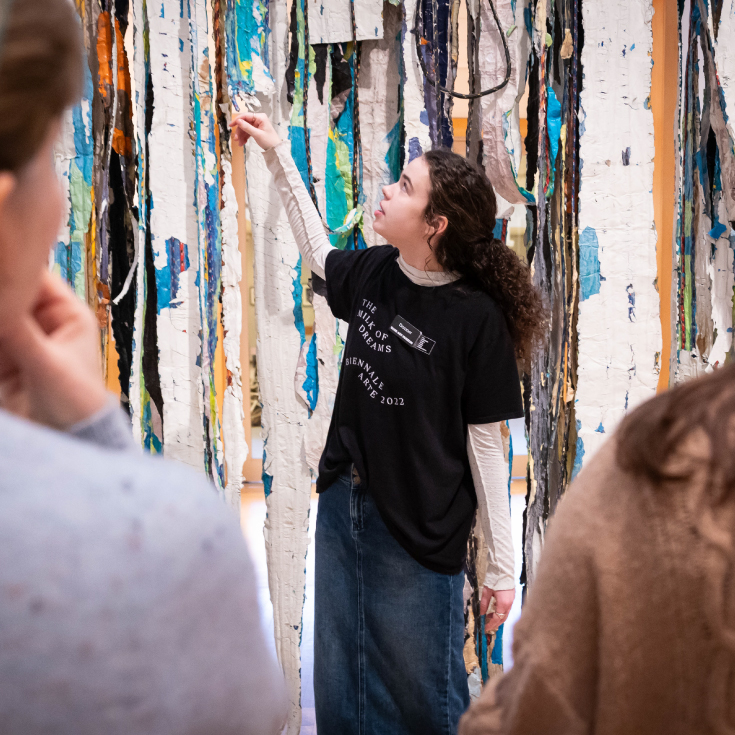 A Brandeis student docent discussing a work of art with a group of visitors.