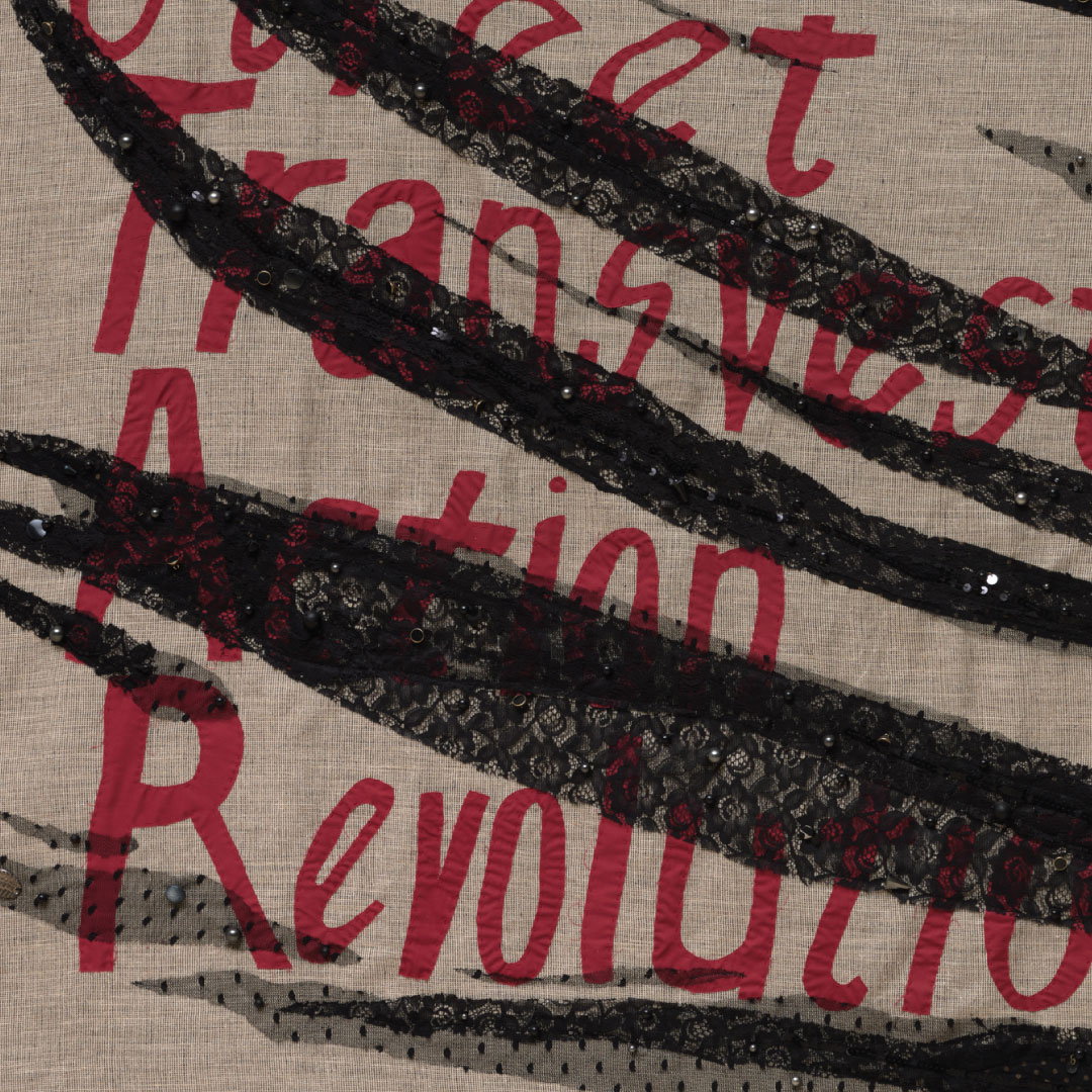 Detail of "Street Transvestites 1973" a textile banner with notions and costume jewelry that says "Street Transvestites Action Revolutionaries"