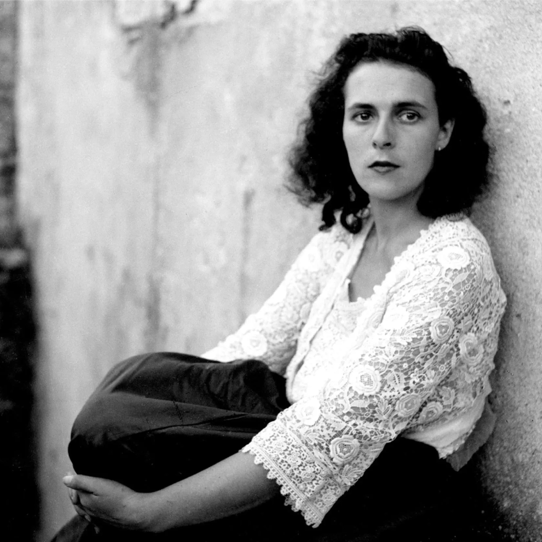 Black and white photograph of a young Leonora Carrington leaning against a wall.